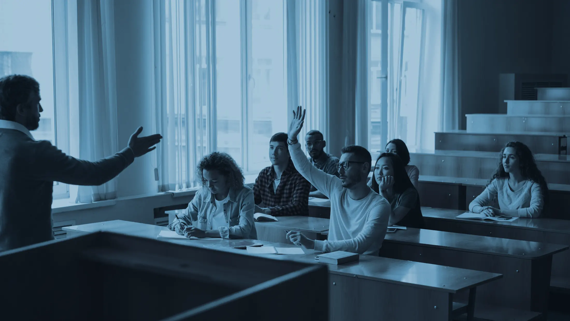 A professor lecturing to a class; a student raises a hand